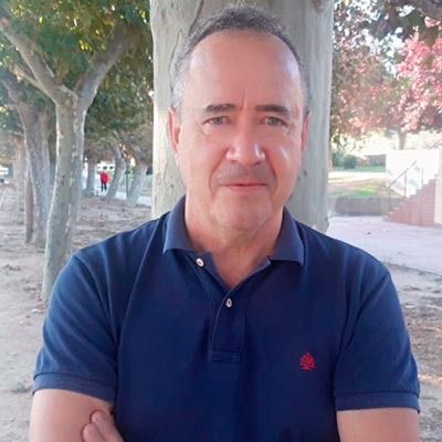 Un hombre con un polo azul está parado frente a un árbol.